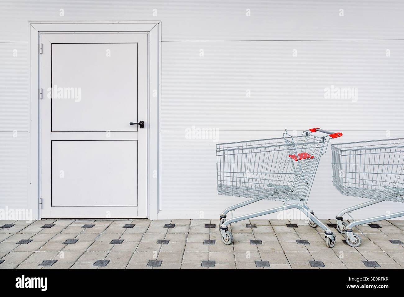 Deux chariots sur un trottoir carrelé contre un mur et une porte blancs propres, scène minimaliste de la vente au détail et de la culture de la consommation, orientation sélective Banque D'Images