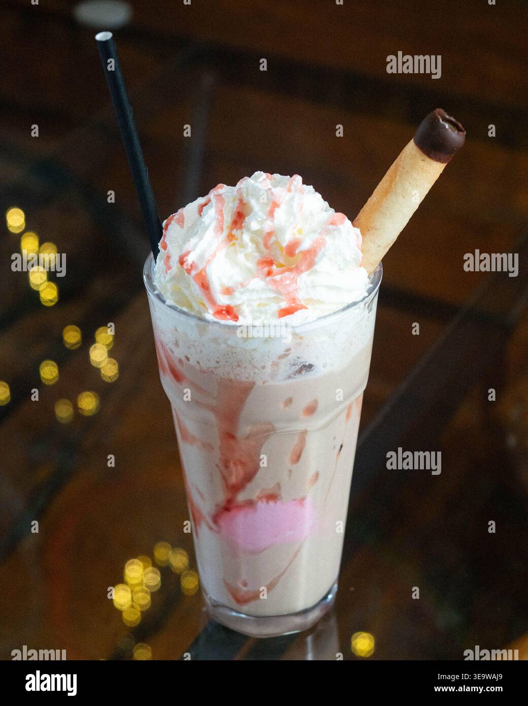 Boisson crémeuse garnie de crème fouettée et de filet de fraise. Les tourbillons de fraise se mélangent avec le lait et la base de crème glacée. Bâton de chocolat et paille noire COM Banque D'Images