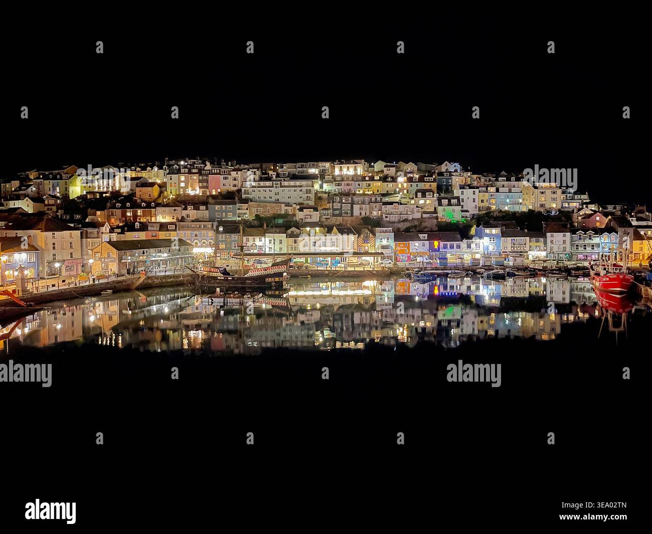 Lumières vives des chalets de bord de mer reflétant les eaux calmes de nuit dans le port de la pittoresque ville balnéaire de Brixham, Devon Banque D'Images