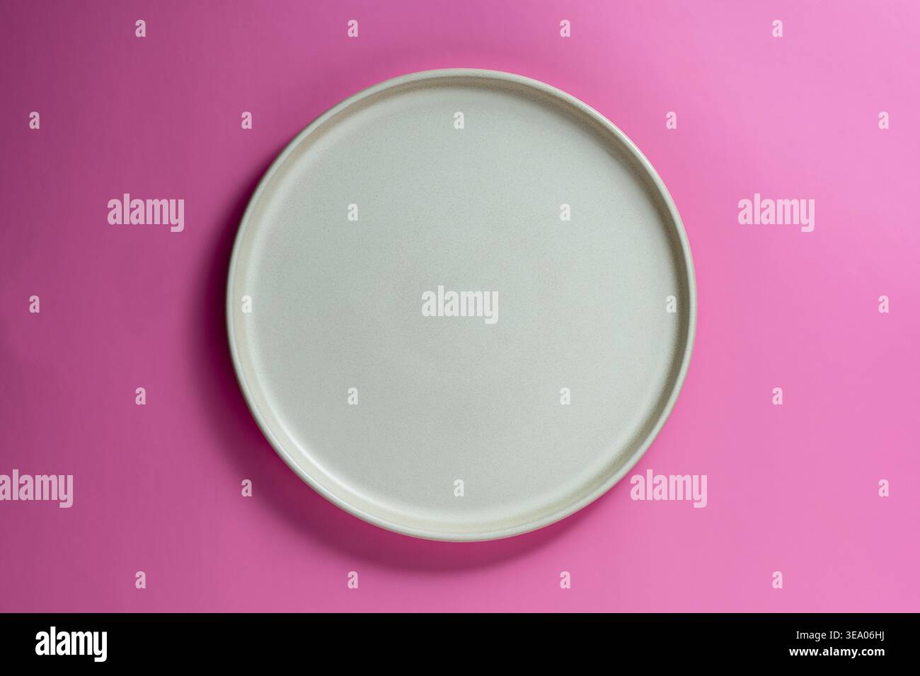 Vue de dessus minimaliste d'une plaque de céramique vide centrée sur une surface rose éclatante, gros plan. Parfait pour les maquettes de menus de restaurant ou culi créatif Banque D'Images