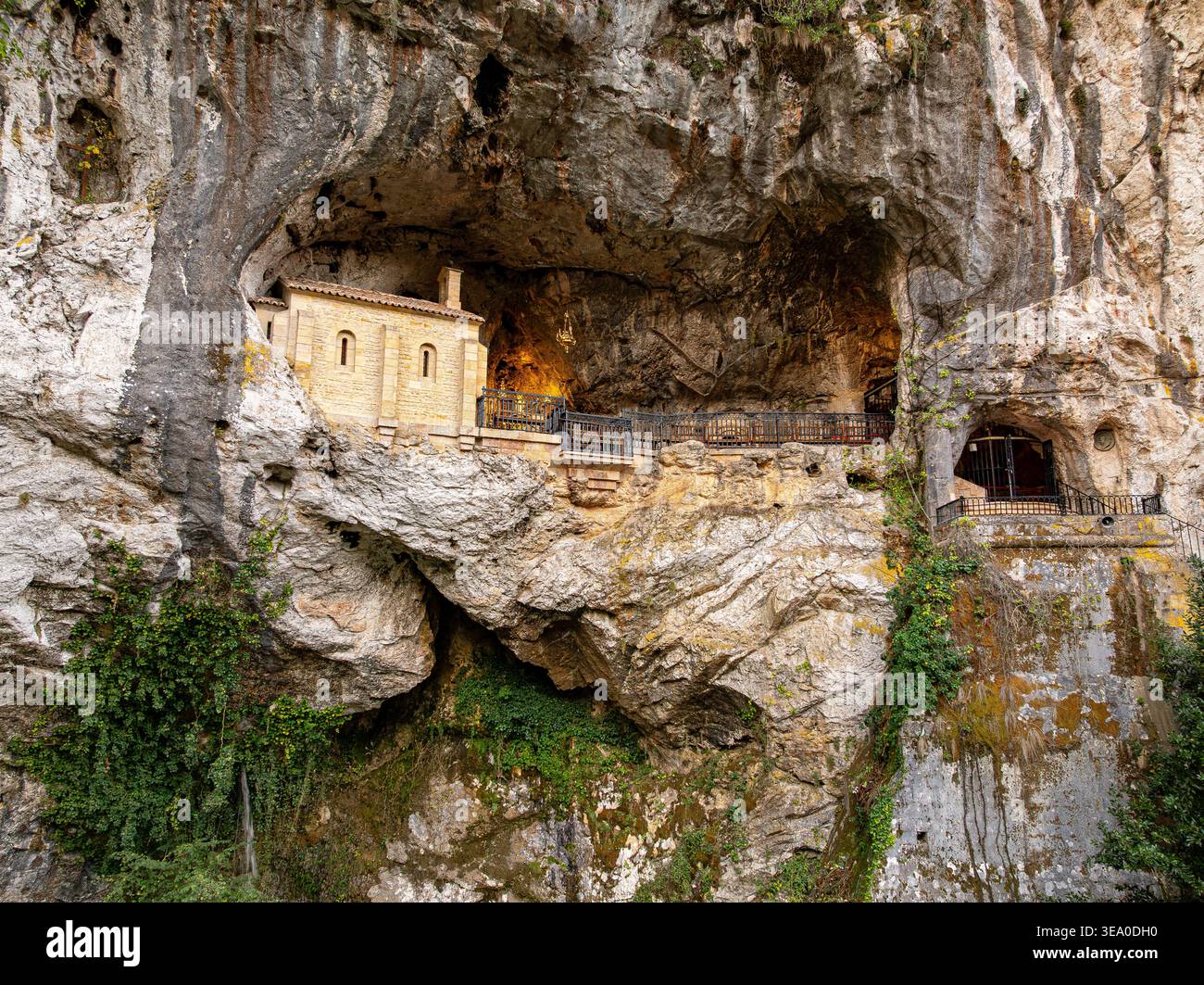 Vue aérienne du Santuario de Covadonga, une basilique nichée dans une grotte, où la lumière chaude contraste avec la pierre grise rugueuse Santa Cueva de CoV Banque D'Images