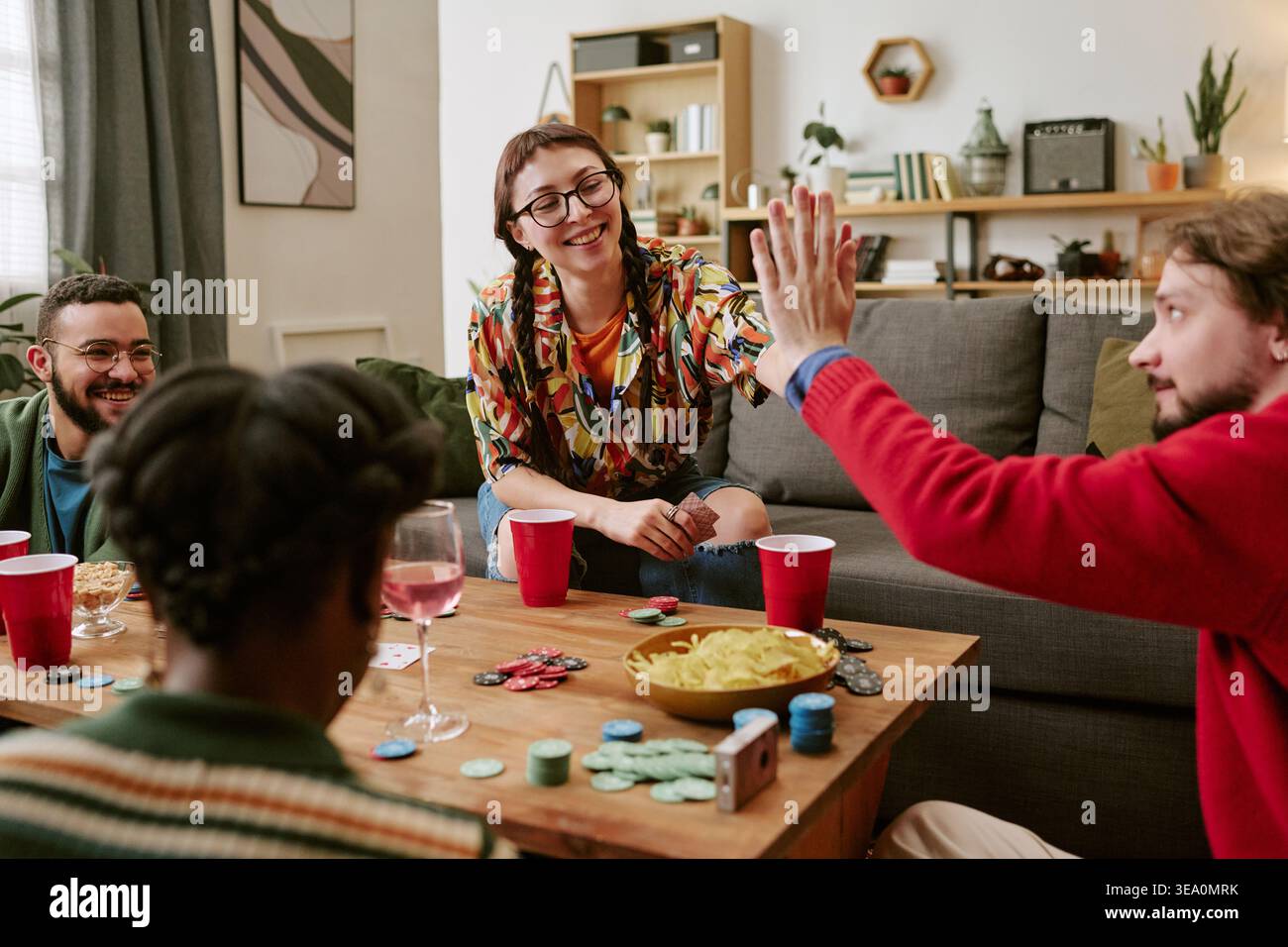 Divers amis jouant au poker et célébrant Win at House Party Banque D'Images