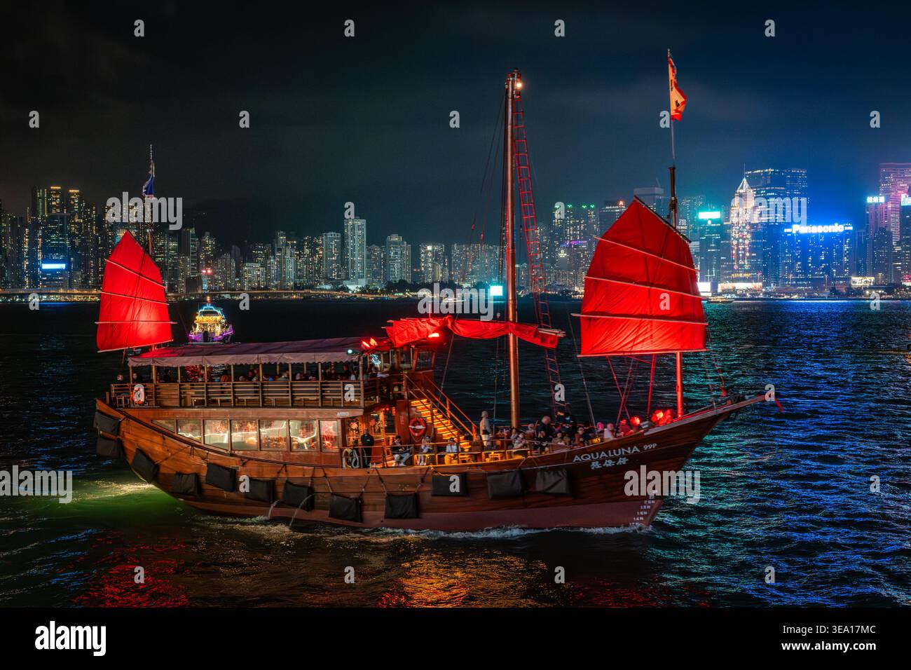 Aqua Luna navigue la nuit sur le port Victoria de Hong Kong pendant le spectacle laser Symphony of Lights avec la ville illuminée en arrière-plan. Banque D'Images