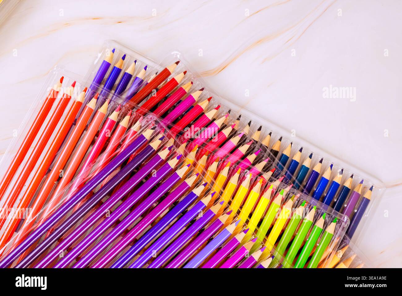 Les crayons de couleur sont placés ensemble dans un emballage transparent sur fond blanc sous lumière naturelle. Banque D'Images