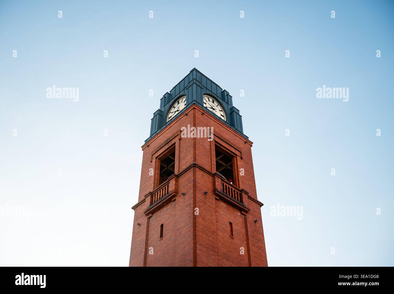 Tour d'horloge en briques rouges de Stary Browar contre ciel bleu clair. Une vue symétrique à angle bas de la tour de brique rouge avec dessus en métal foncé avec horloge classique Banque D'Images