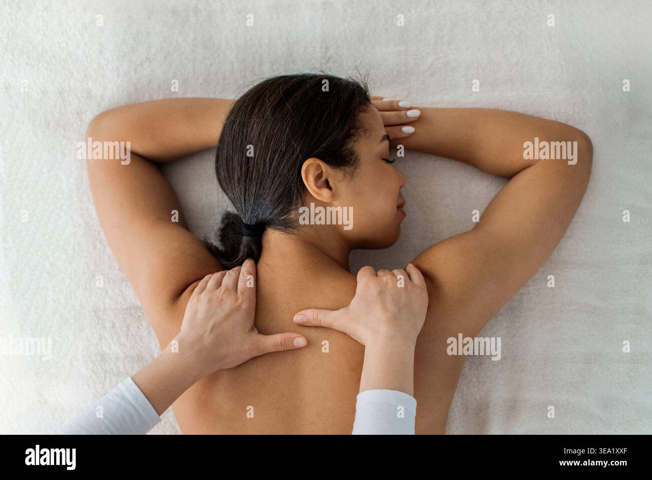 Thérapeute effectuant un massage des tissus profonds sur le haut du dos de la jeune femme noire Banque D'Images