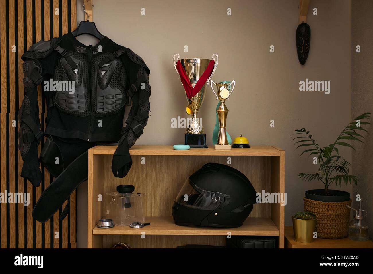 Gros plan de l'équipement de protection de moto suspendu à côté des trophées et du casque sur l'étagère, présentant les réalisations de sport automobile et le concept de sécurité. Convient pour la promotion des clubs de course ou les annonces d'entraînement Banque D'Images