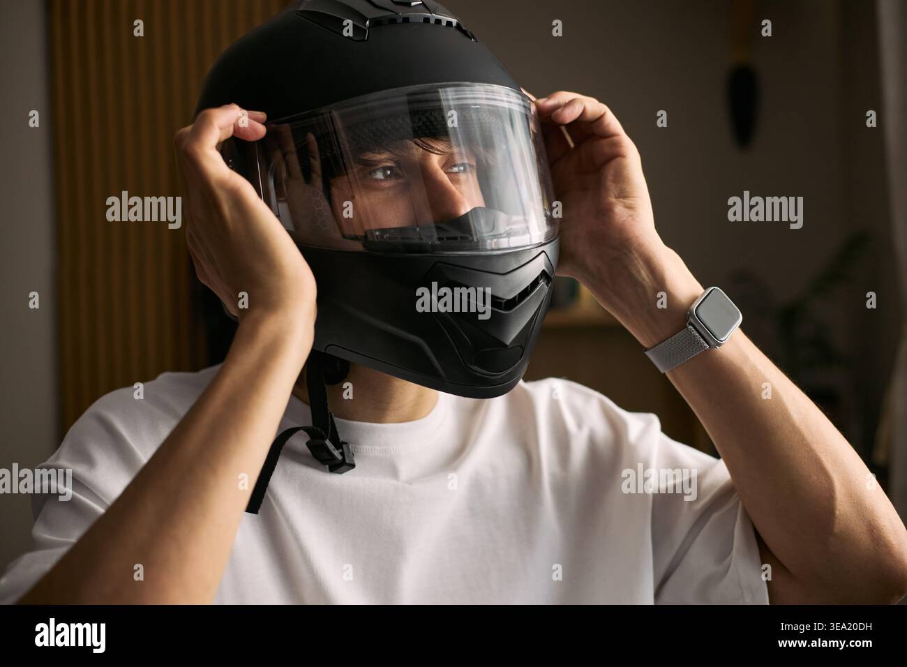 Jeune homme asiatique adulte ajustant le casque de moto avant de rouler, mettant l'accent sur la sécurité routière et la mobilité personnelle. Utile pour l'assurance transport, la formation des cavaliers, les campagnes de navettage Banque D'Images