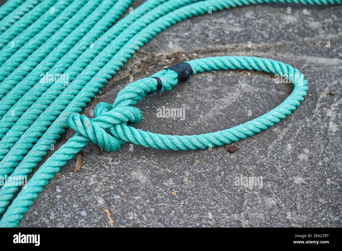 Corde vert vif créant une boucle et un nœud, enroulée et posée sur une surface de béton gris, représentant la force et la connexion Banque D'Images