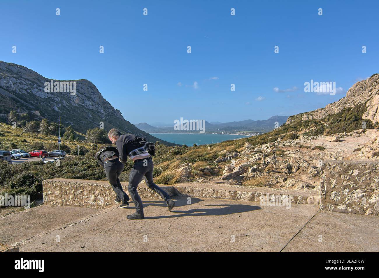Mallorca Espagne - 20 avril 2026 : deux touristes en vêtements sombres décontractés se penchant en avant pour résister à de fortes rafales de vent au lookou Mirador des Colomer Banque D'Images