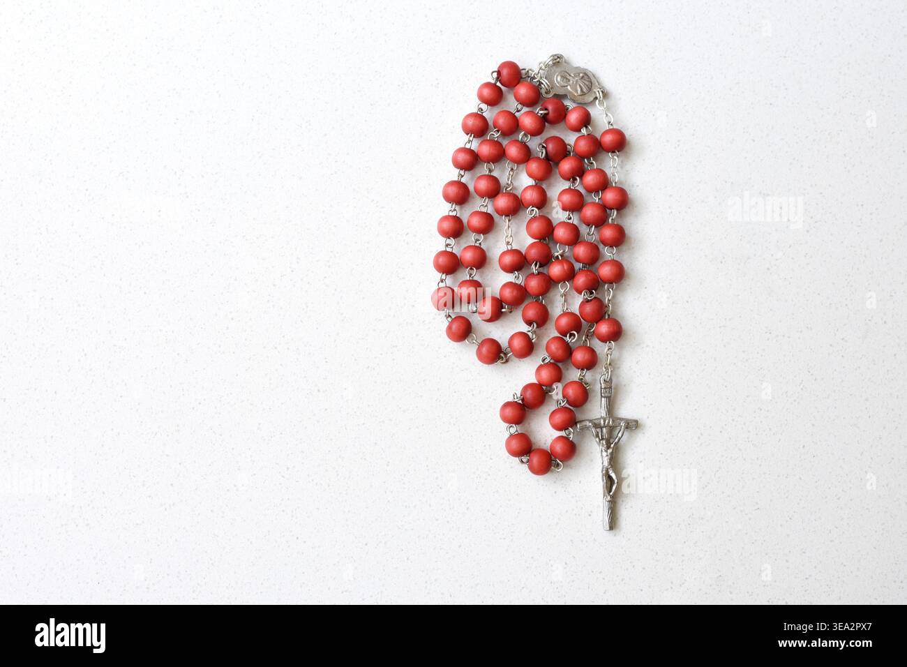 Vue de dessus d'un chapelet rouge placé sur une table blanche propre. Composition minimaliste mettant en valeur le symbolisme religieux, le contraste des couleurs et la signification spirituelle Banque D'Images
