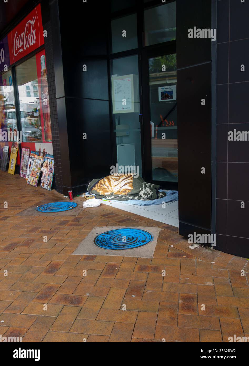 Tauranga Nouvelle-Zélande 19 avril 2026 ; personne dormant rude sous une couverture à motifs dans une porte de magasin, la représentation visuelle de av Enduring Homele Banque D'Images