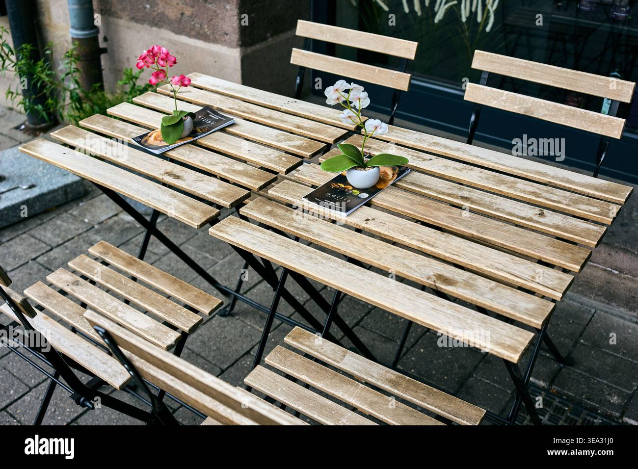 Tables pliantes en bois vides et chaises d'une terrasse de café en plein air, décorées de petits pots de fleurs et de menus sur un trottoir de la ville. Banque D'Images