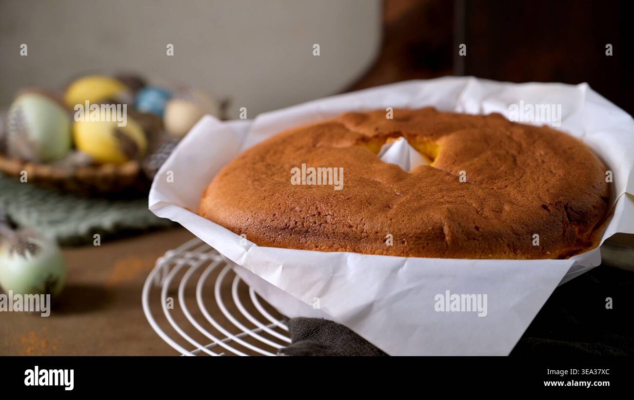 Le gâteau éponge portugais fraîchement cuit repose sur une grille métallique dans sa doublure en papier. Une lumière naturelle douce met en valeur la texture aérée et les setti de vacances rustiques Banque D'Images