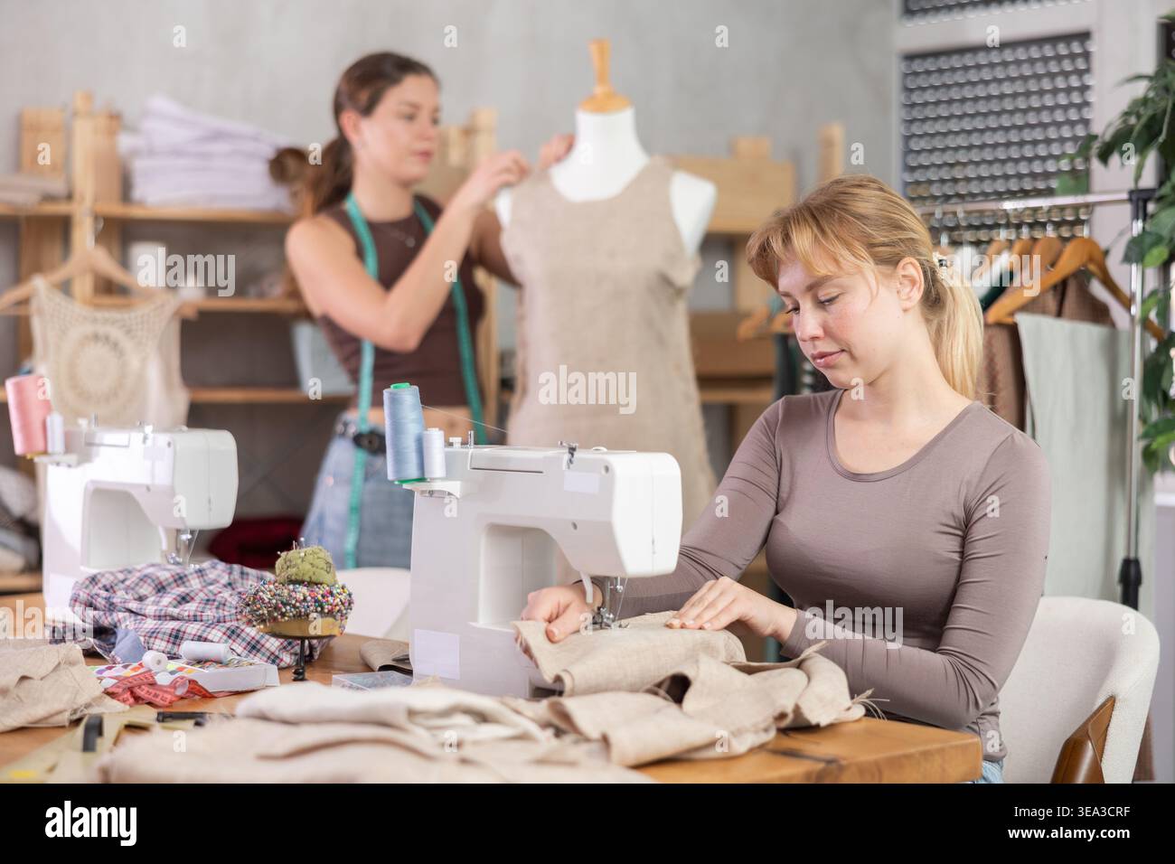 Tailleur femme travaillant sur une machine à coudre avec un assistant en arrière-plan Banque D'Images