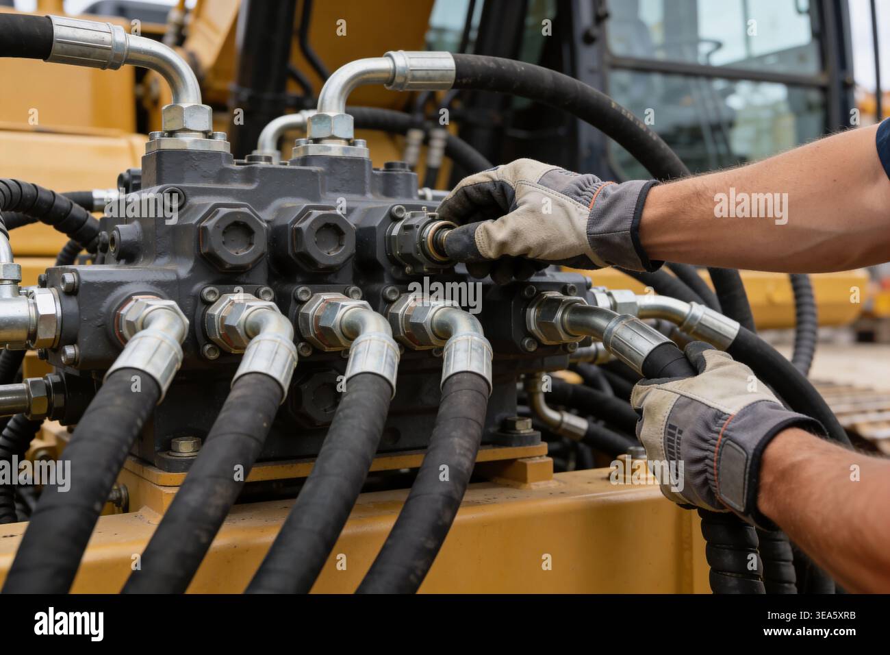 Gros plan de mains gantées fixant des raccords métalliques et des flexibles haute pression à un collecteur hydraulique sur un chantier de construction Banque D'Images