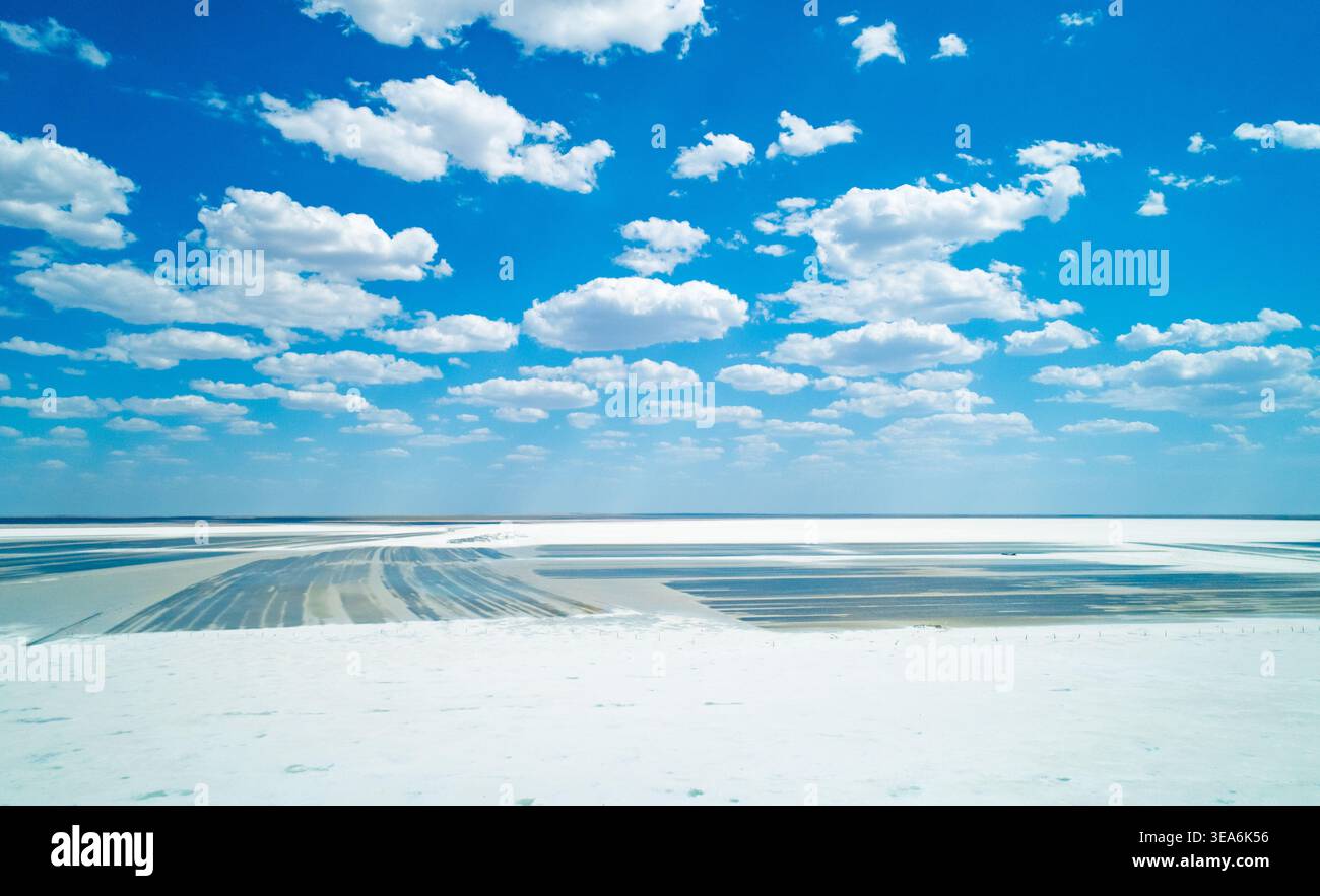 Vaste paysage salé au lac Baskunchak avec des motifs miniers distincts sous un ciel bleu vif et des nuages blancs dispersés Banque D'Images
