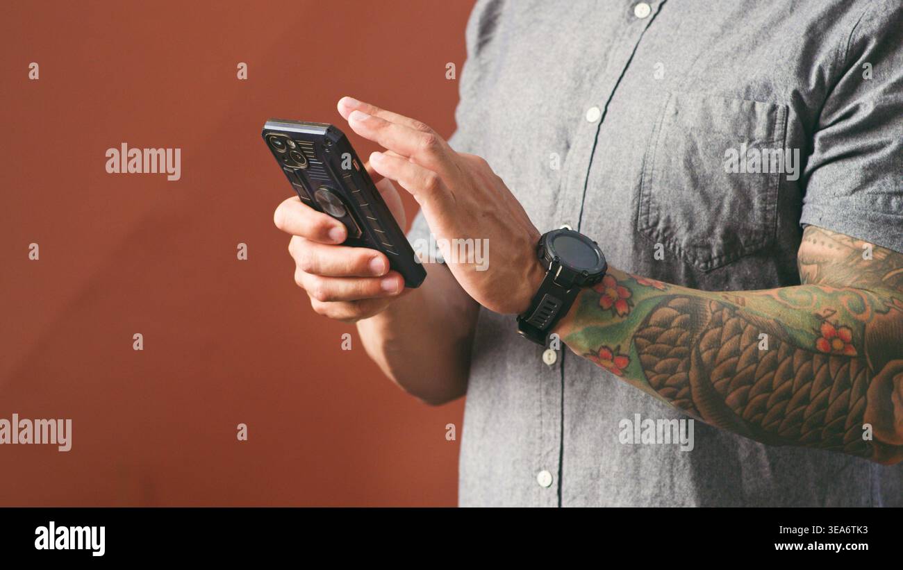 Homme tatoué à l'aide d'un smartphone avec Smartwatch dans une chemise décontractée - gros plan des mains texturant Banque D'Images