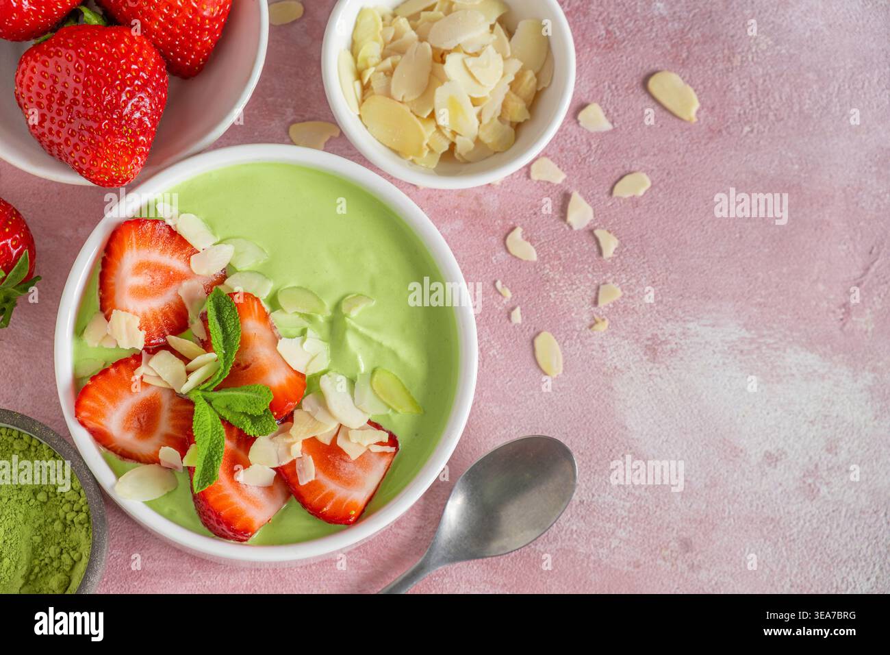 Yogourt matcha vert crémeux servi avec des fraises tranchées et des flocons d'amandes dans un bol avec cuillère. Vue de dessus avec espace de copie. Dessert sain, protéines Banque D'Images