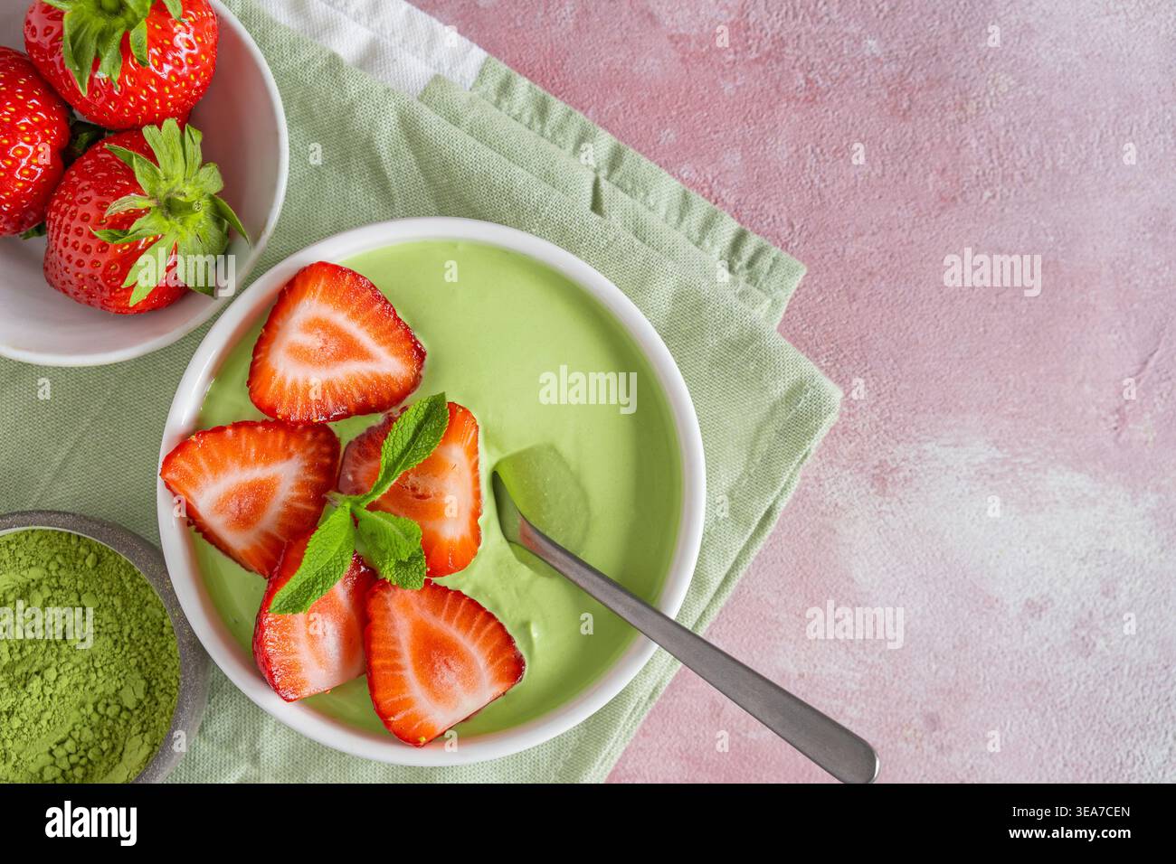 Yogourt Matcha garni de fraises fraîches et de feuilles de menthe dans un bol avec une cuillère. Vue de dessus avec espace de copie. Dessert sain, petit déjeuner smoothie vert Banque D'Images