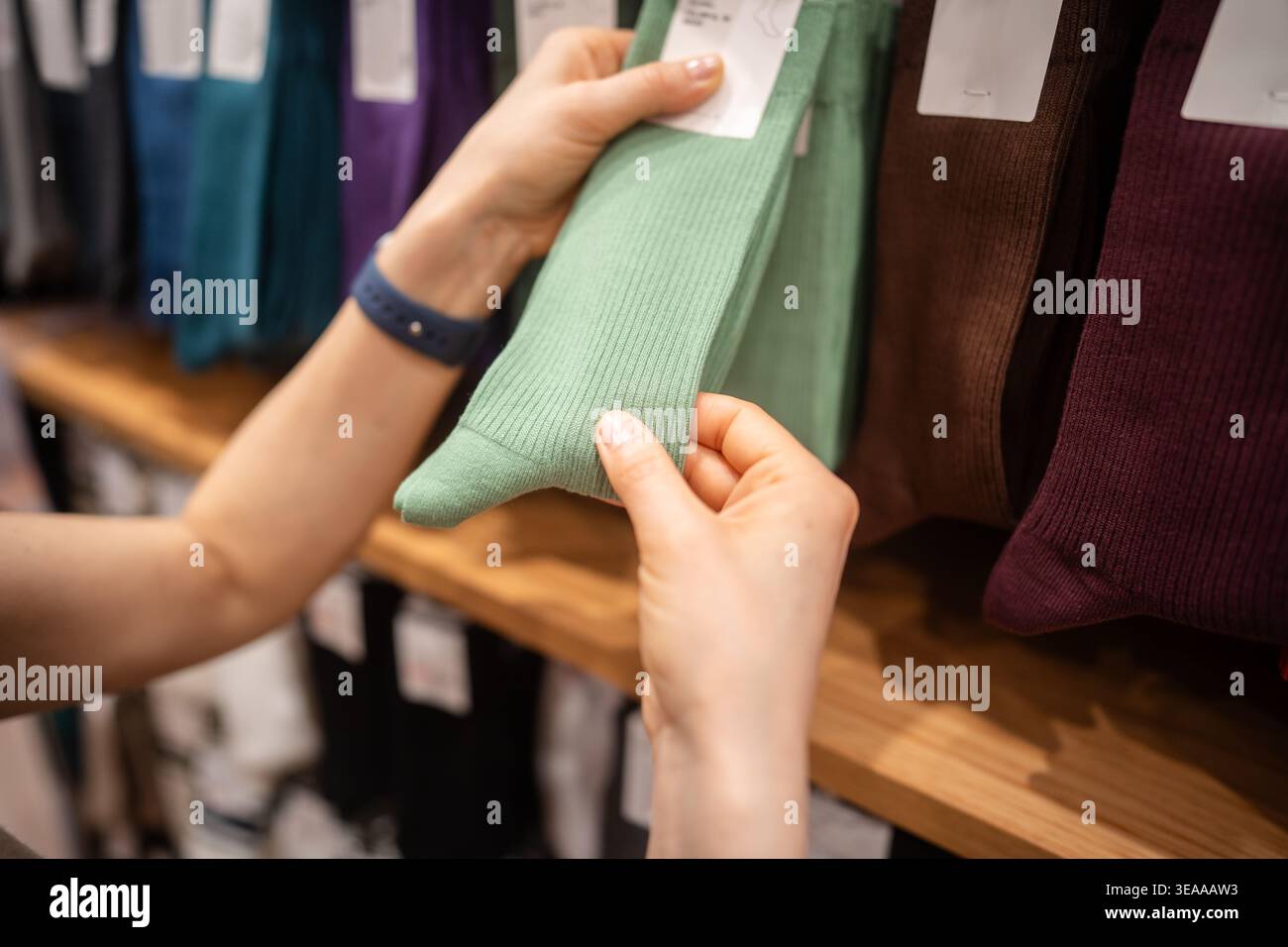 Client féminin magasinant dans le magasin de vêtements de mode, cueillant la paire de chaussettes sur l'affichage de cintre. Banque D'Images