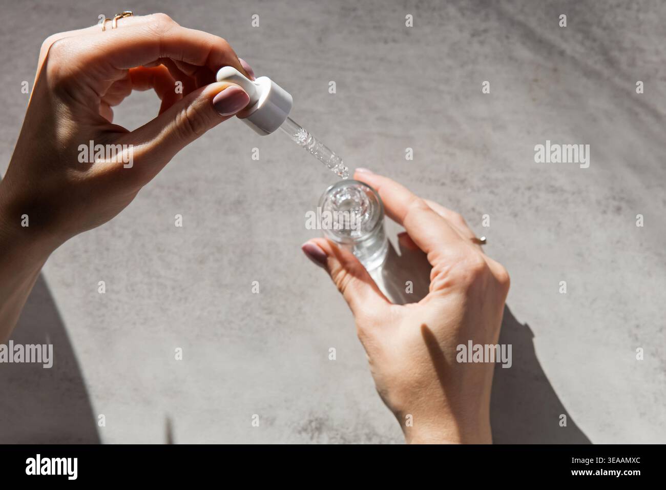 Gros plan des mains à l'aide d'un compte-gouttes pour appliquer le sérum d'une bouteille en verre. Banque D'Images