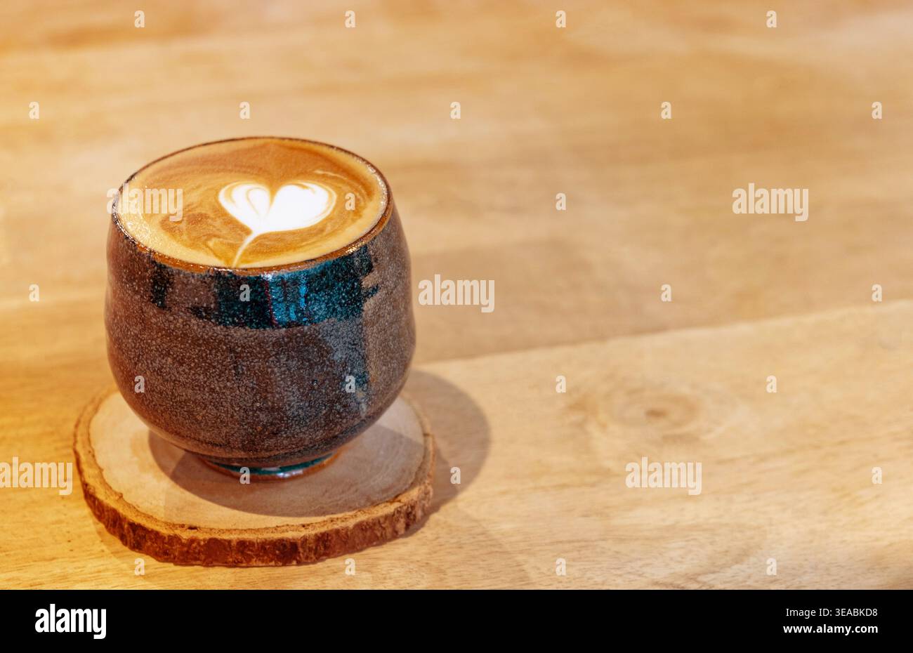Vue latérale du cœur chaud de latte art dans une tasse en céramique émaillée sombre sur des dessous de verre en bois. Style café minimaliste japonais avec grand espace copie en bois. Mots-clés (46 Banque D'Images
