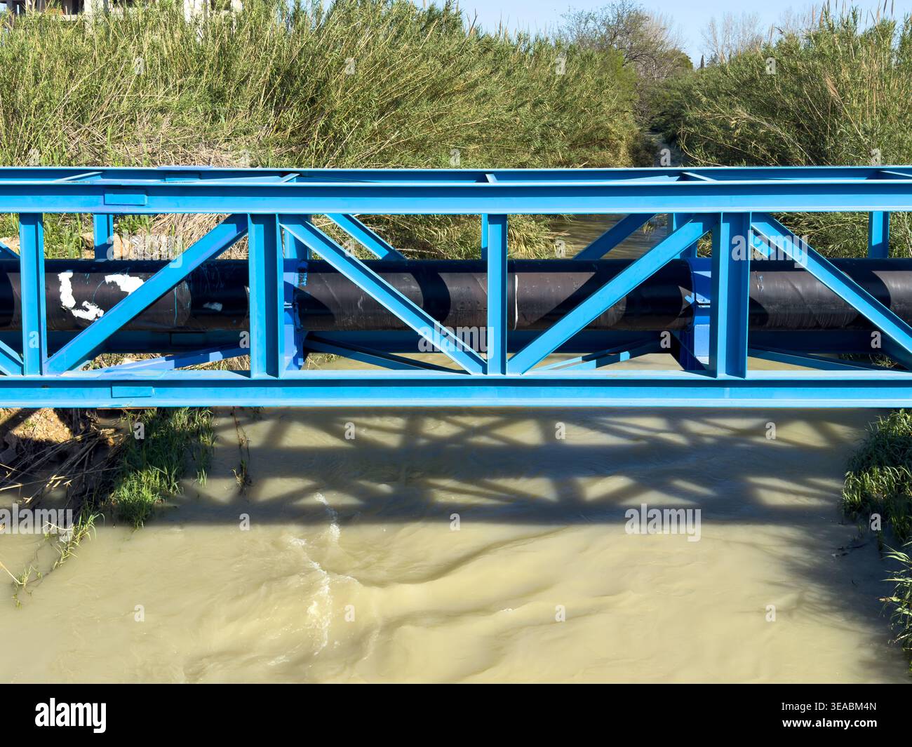 Pont en treillis d'acier bleu soutenant un grand pipeline industriel au-dessus d'une rivière qui coule Banque D'Images