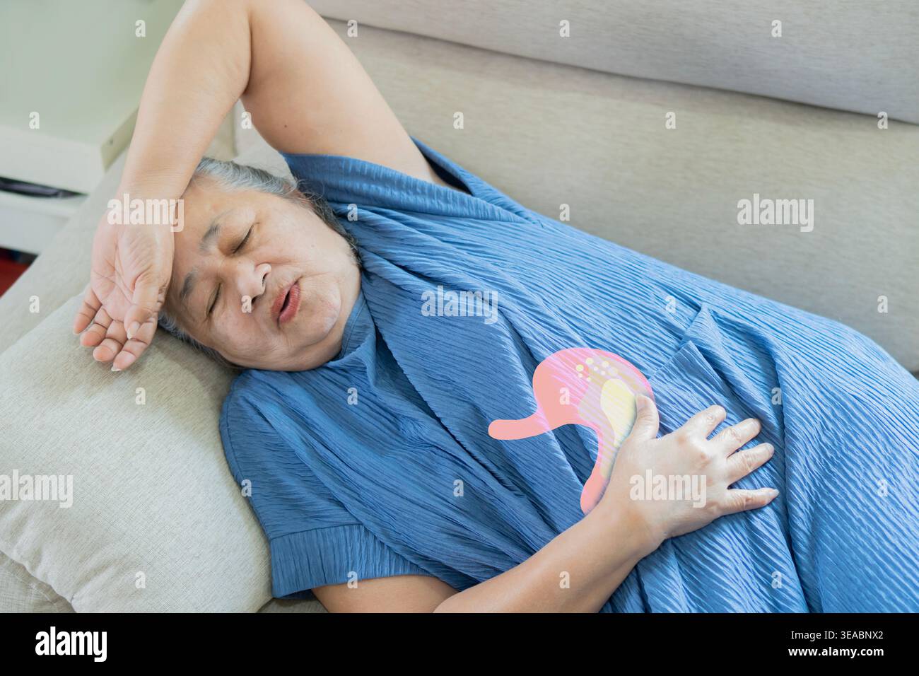 Femme âgée dormant sur un canapé et souffrant de douleurs abdominales sévères, tenant son abdomen dans l'inconfort à la maison. Concept de soins aux personnes âgées. Banque D'Images