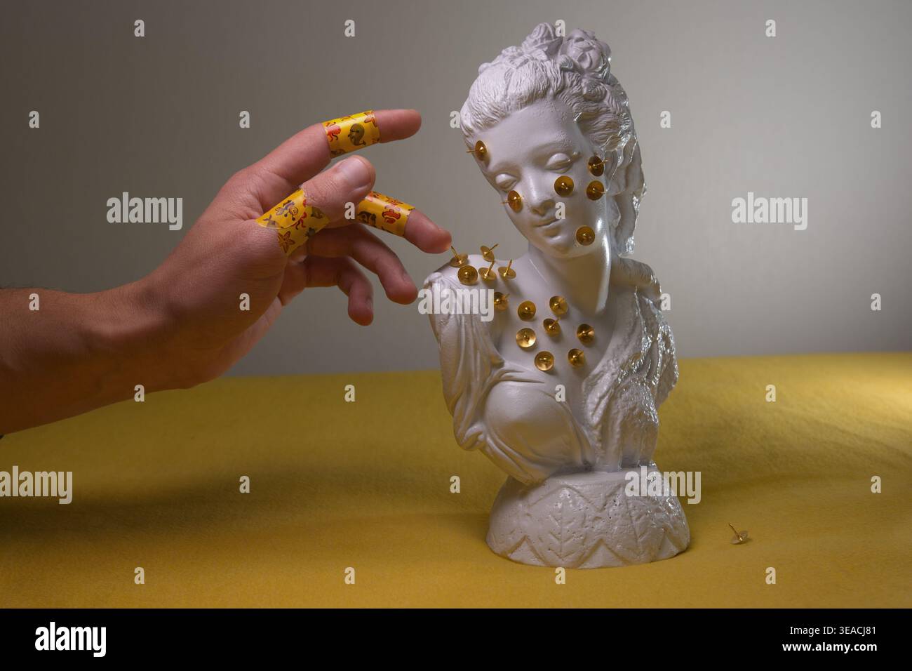 Nature morte conceptuelle : buste de gypse blanc avec des épingles dorées et une main humaine avec des bandages colorés. Thèmes de la santé mentale, du traumatisme et de la guérison. Banque D'Images