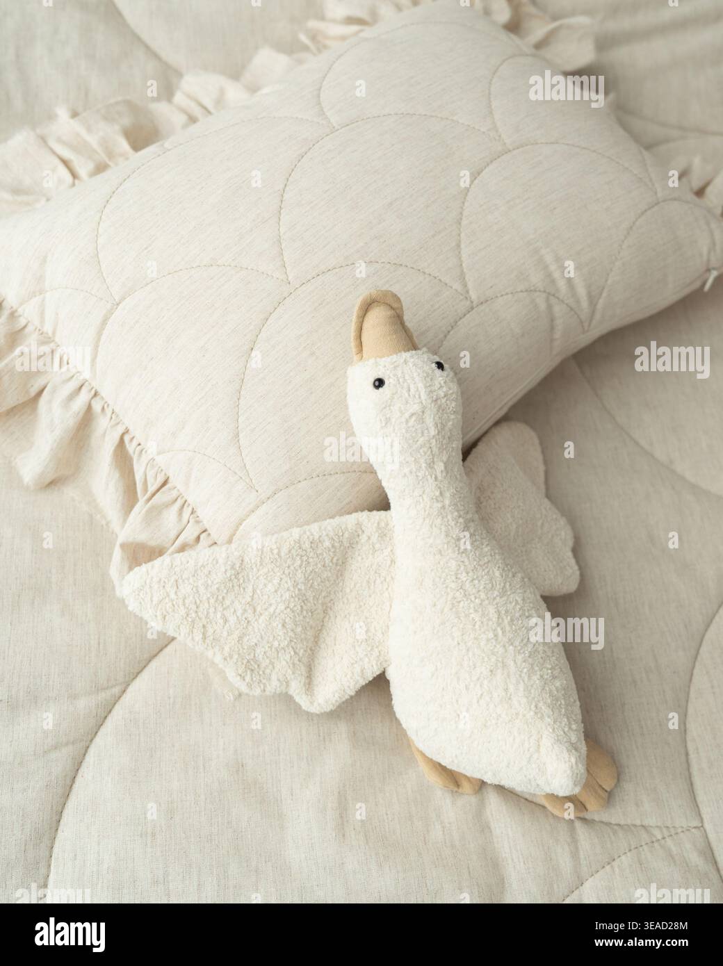 Jouet d'oie en peluche doux placé sur un oreiller confortable. Scène de pépinière minimale avec des tons chauds et une atmosphère calme. Banque D'Images