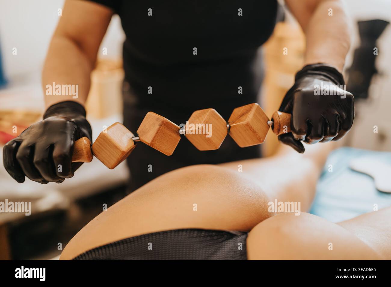 Thérapeute utilisant le rouleau en bois pour le massage profond des tissus sur le dos du client dans le centre de beauté Banque D'Images