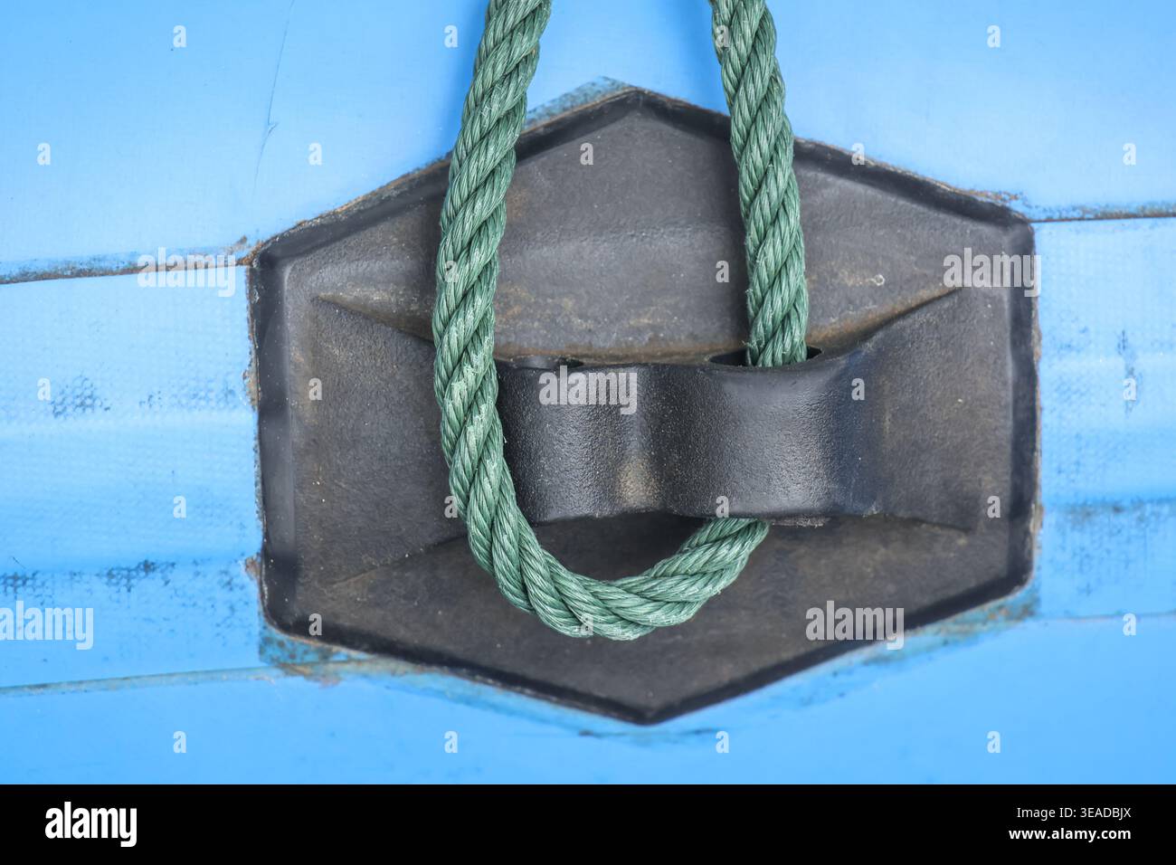 Vue rapprochée de la corde verte attachée solidement à la cale métallique noire sur la surface bleue montrant une connexion solide et la stabilité dans les conditions nautiques de convoyage s. Banque D'Images