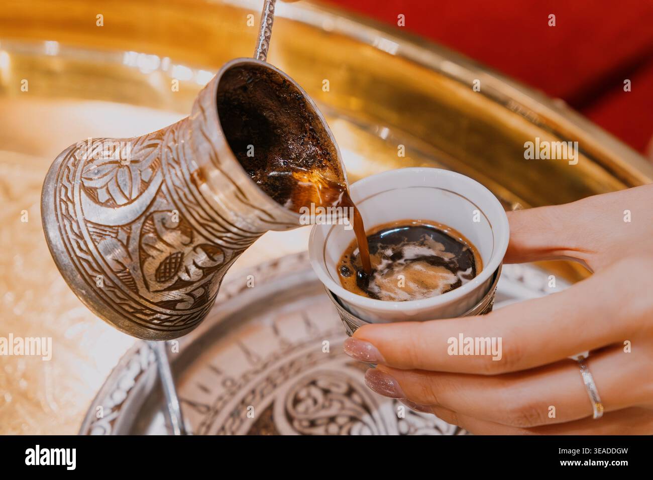 Mains de femme versant du café turc chaud frais d'un cezve en métal classique dans une petite tasse traditionnelle, montrant une boisson culturelle Banque D'Images