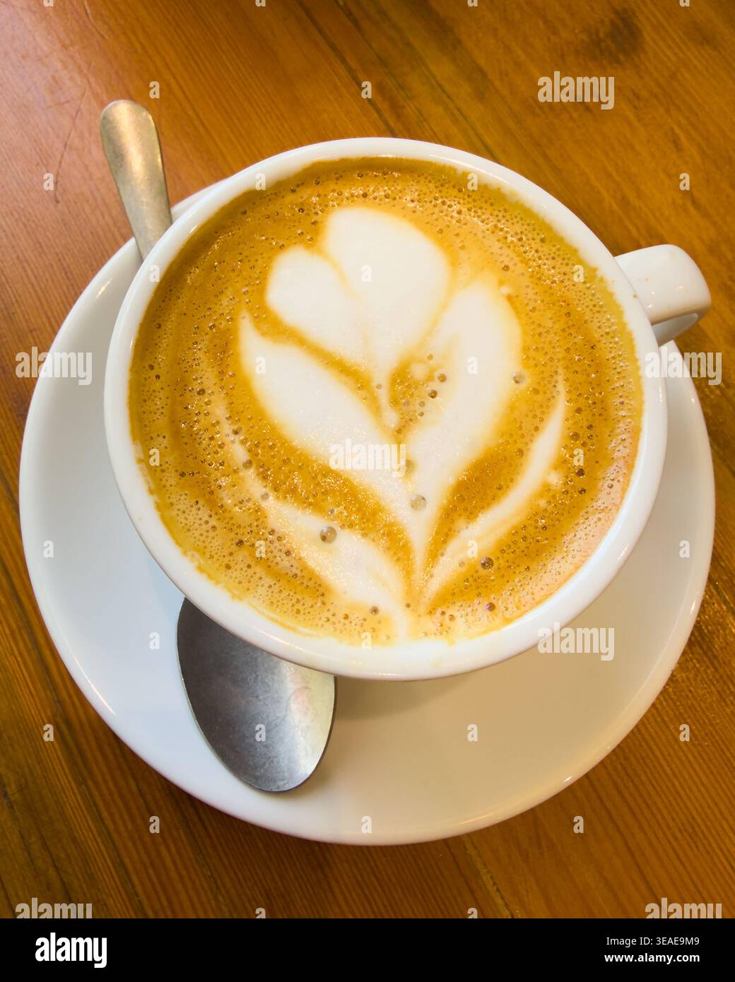 Motif floral sur la surface du café dans une tasse blanche avec sppelle et soucoupe sur la surface en bois Banque D'Images