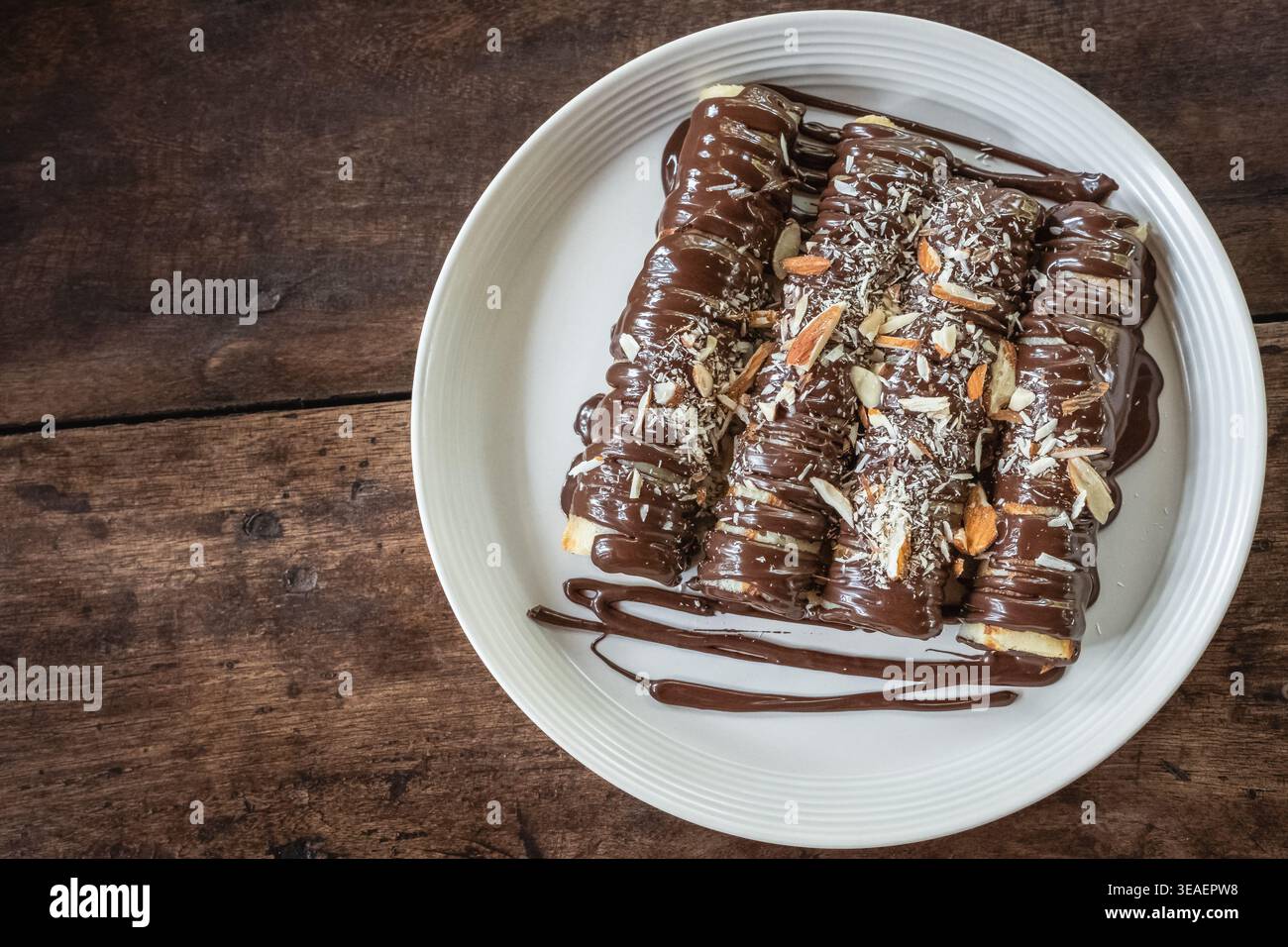 Gros plan photo de délicieuses crêpes à la sauce au chocolat et saupoudrées d'amandes sur une plaque blanche sur une planche de bois rustique. Crêpes de dessert fines, rouleau Banque D'Images