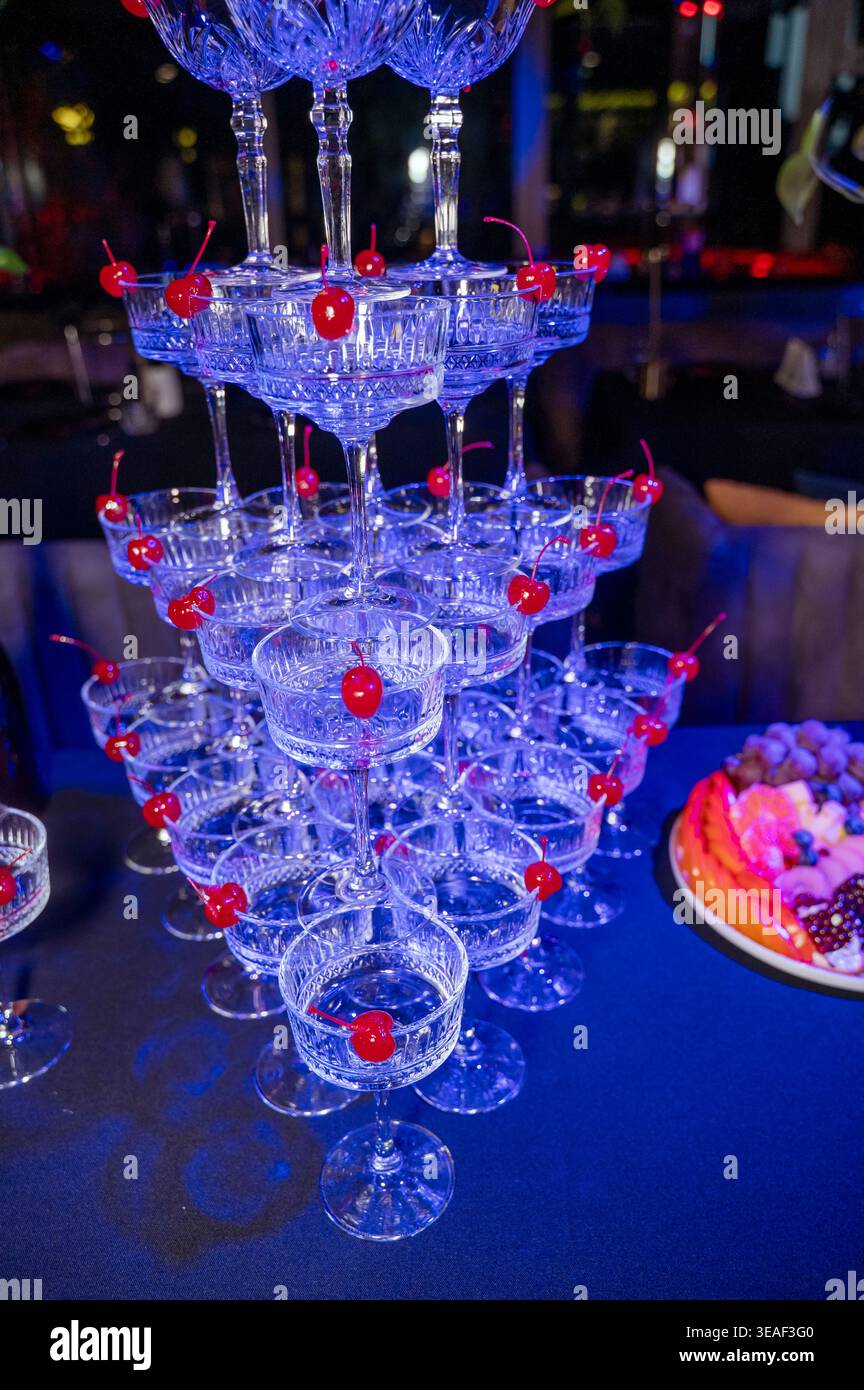 Gros plan de la pyramide de verre avec garniture de cerise maraschino rouge sous la lumière bleue Banque D'Images