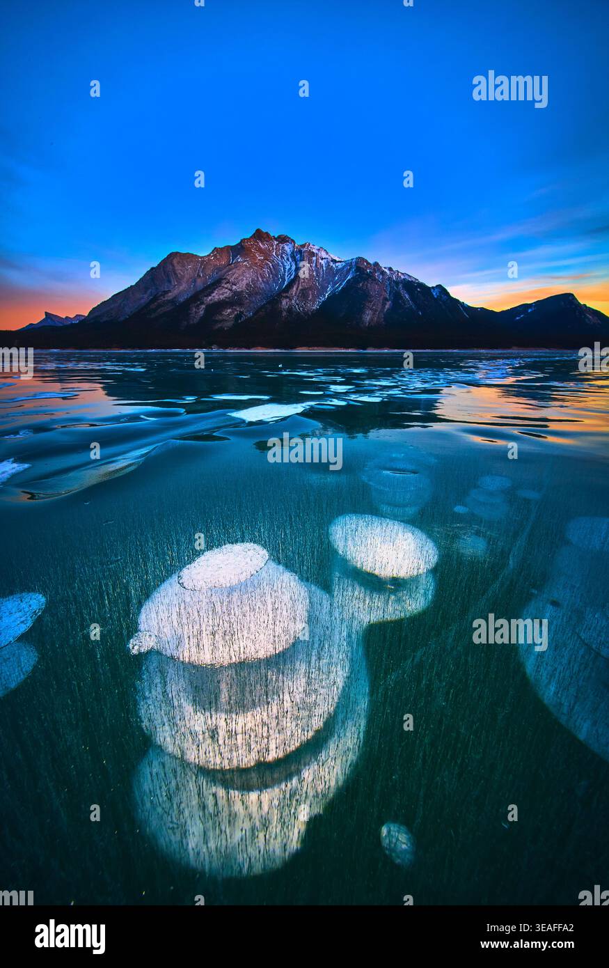 Bulles de méthane gelées et reflets de montagne sur Winter Lake au coucher du soleil Banque D'Images