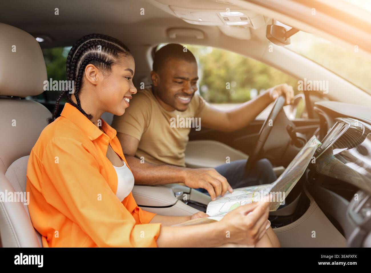 Jeune couple noir souriant tout en regardant la carte papier ensemble dans la voiture Banque D'Images