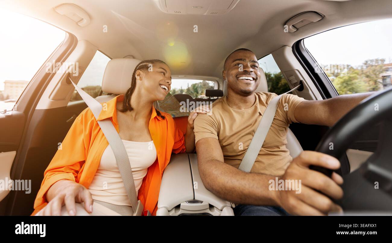 Jeune couple afro-américain appréciant conduire ensemble, souriant en voiture Banque D'Images