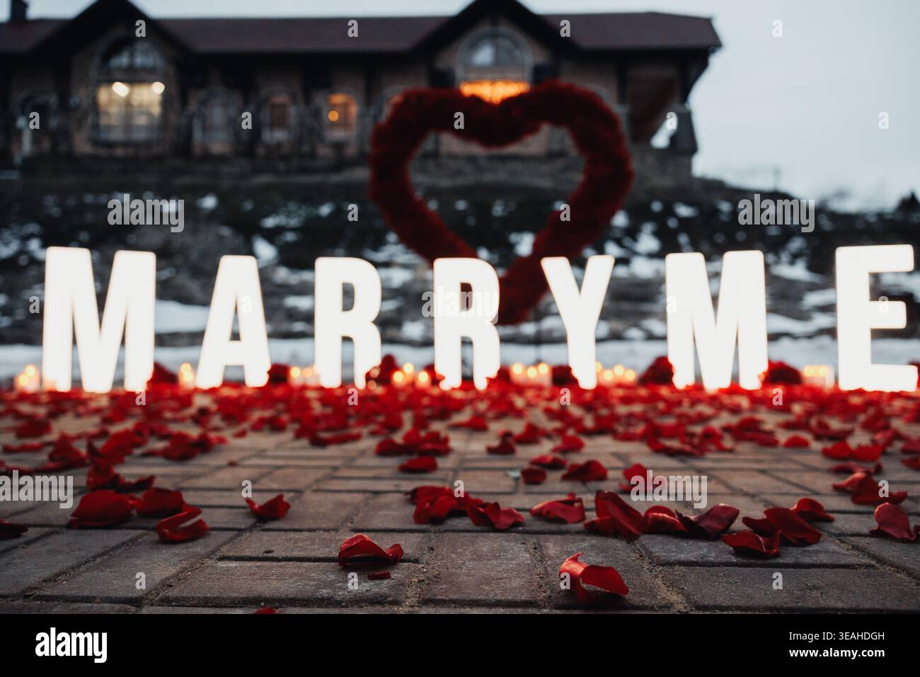 Présentation de proposition en gros plan avec couronne de coeur et lettres MARRY ME illuminées, pétales de rose dispersés sur des planches de bois, éclat dramatique et rouge vif Banque D'Images