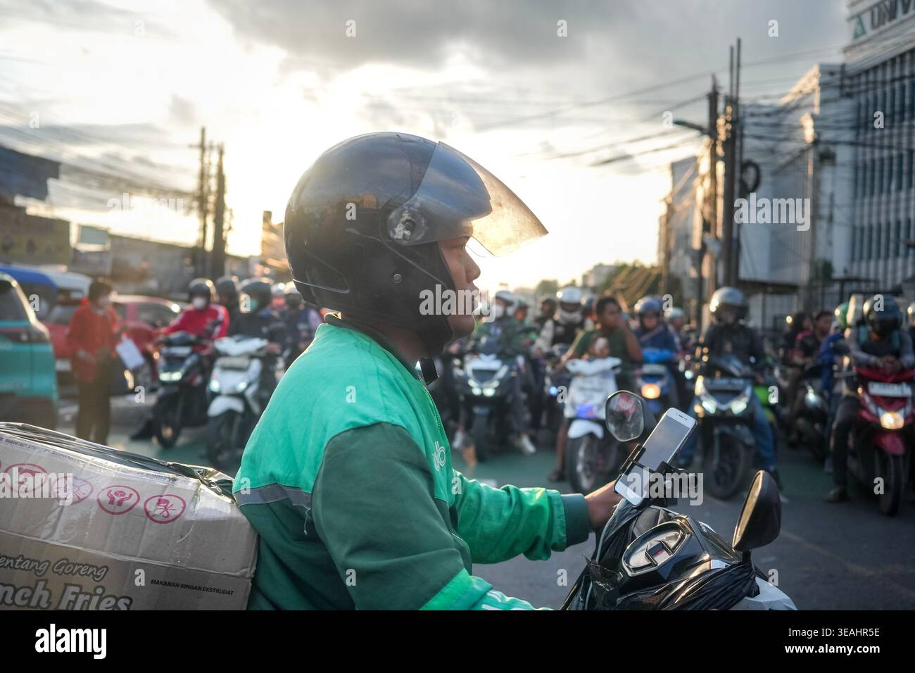 Jakarta, Indonésie - 2 février 2026 - profil latéral d'un livreur sur une moto transportant un colis, naviguant à travers de lourdes heures de pointe tra Banque D'Images
