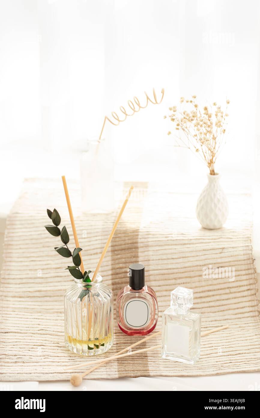 Une sélection de flacons de parfum et un diffuseur de roseau reposent sur une nappe de couleur crème, entourés de fleurs délicates et d'une sculpture en fil d'or. Banque D'Images