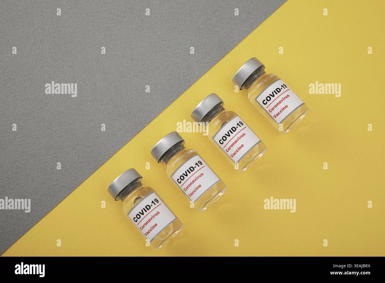 Quatre flacons vides de vaccin COVID-19 sont disposés sur une surface jaune et grise. Banque D'Images