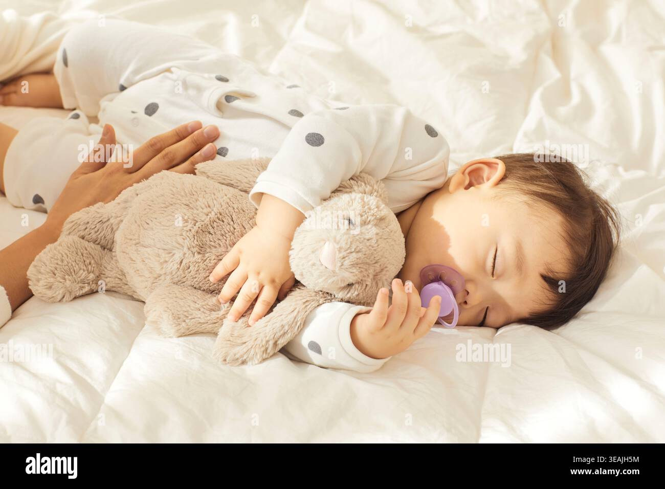 Un bébé endormi est allongé dans le lit, berçant un lapin en peluche et une sucette. Banque D'Images