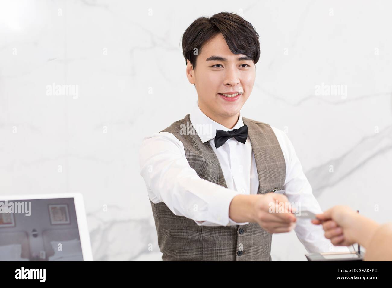 Un jeune homme asiatique souriant réceptionniste d'hôtel remet une carte-clé de chambre à un client. Banque D'Images