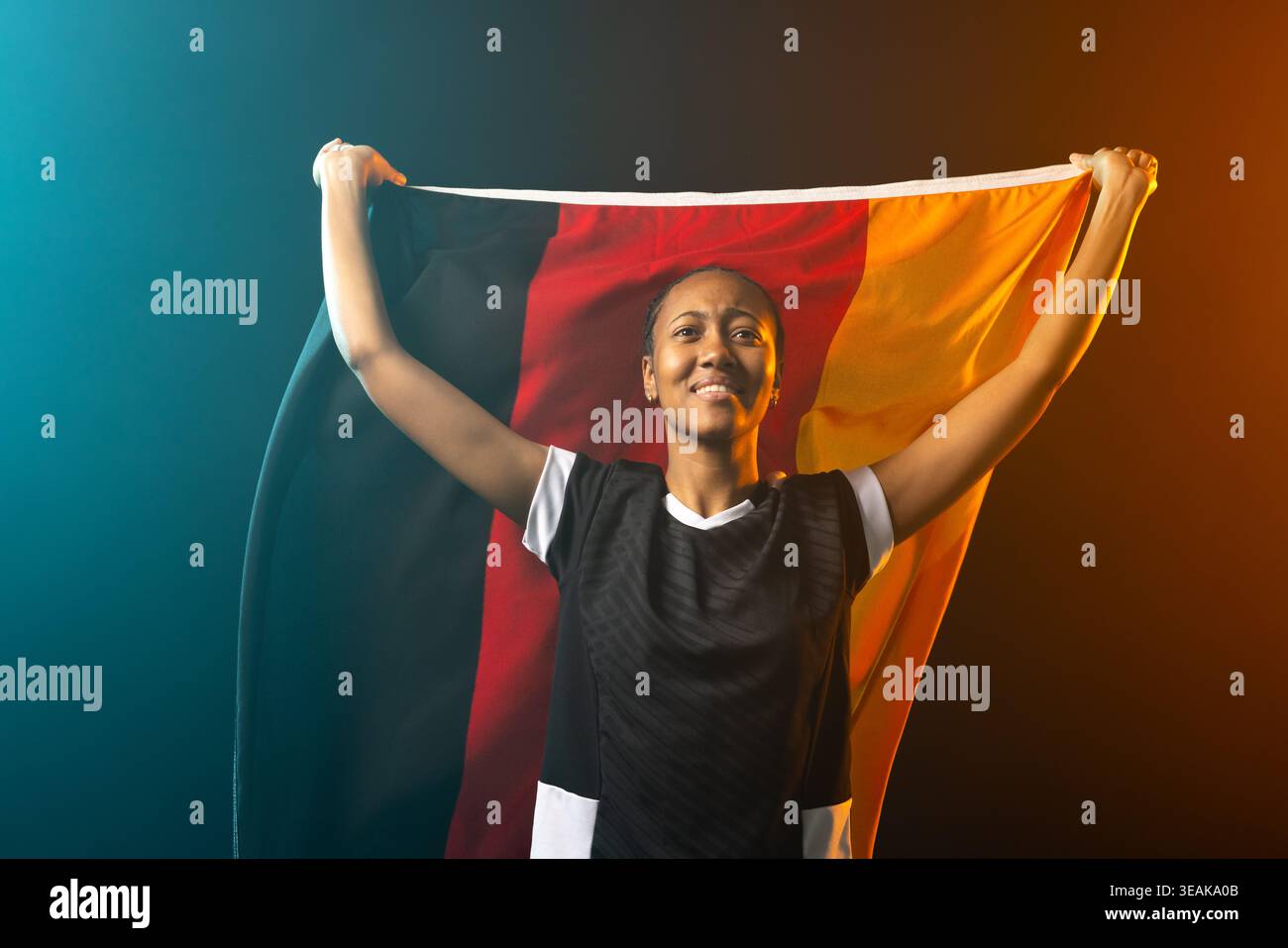 Femme afro-américaine portant une chemise de sport noire tenant le drapeau tricolore au-dessus de la tête dans l'éclairage de studio. Bannière, athlète, jante, sarcelle, orange, toile de fond Banque D'Images