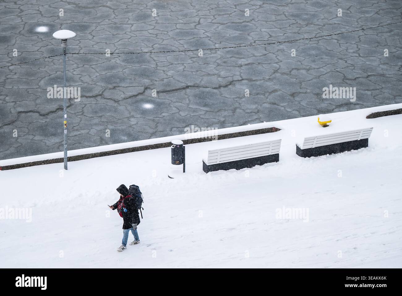 Tallinn, Estonie - 03 janvier 2025 : vue d'une figure solitaire qui traverse le paysage enneigé, contraste frappant avec la mer gelée et les bancs. Banque D'Images