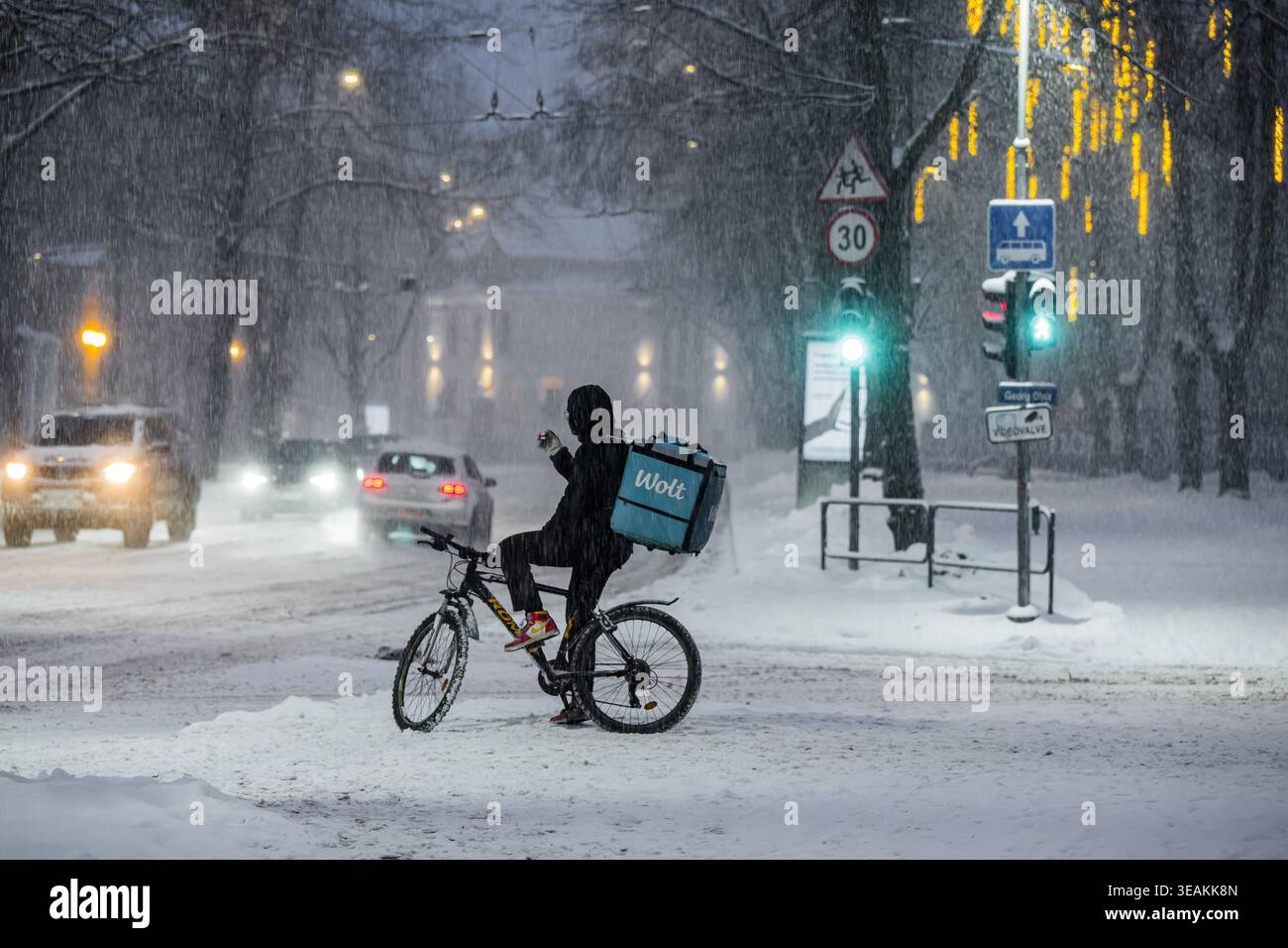 Tallinn, Estonie - 03 janvier 2025 : vue d'un cycliste bravant les fortes chutes de neige près d'un feu de circulation, avec des voitures naviguant sur les routes glissantes sous le Banque D'Images