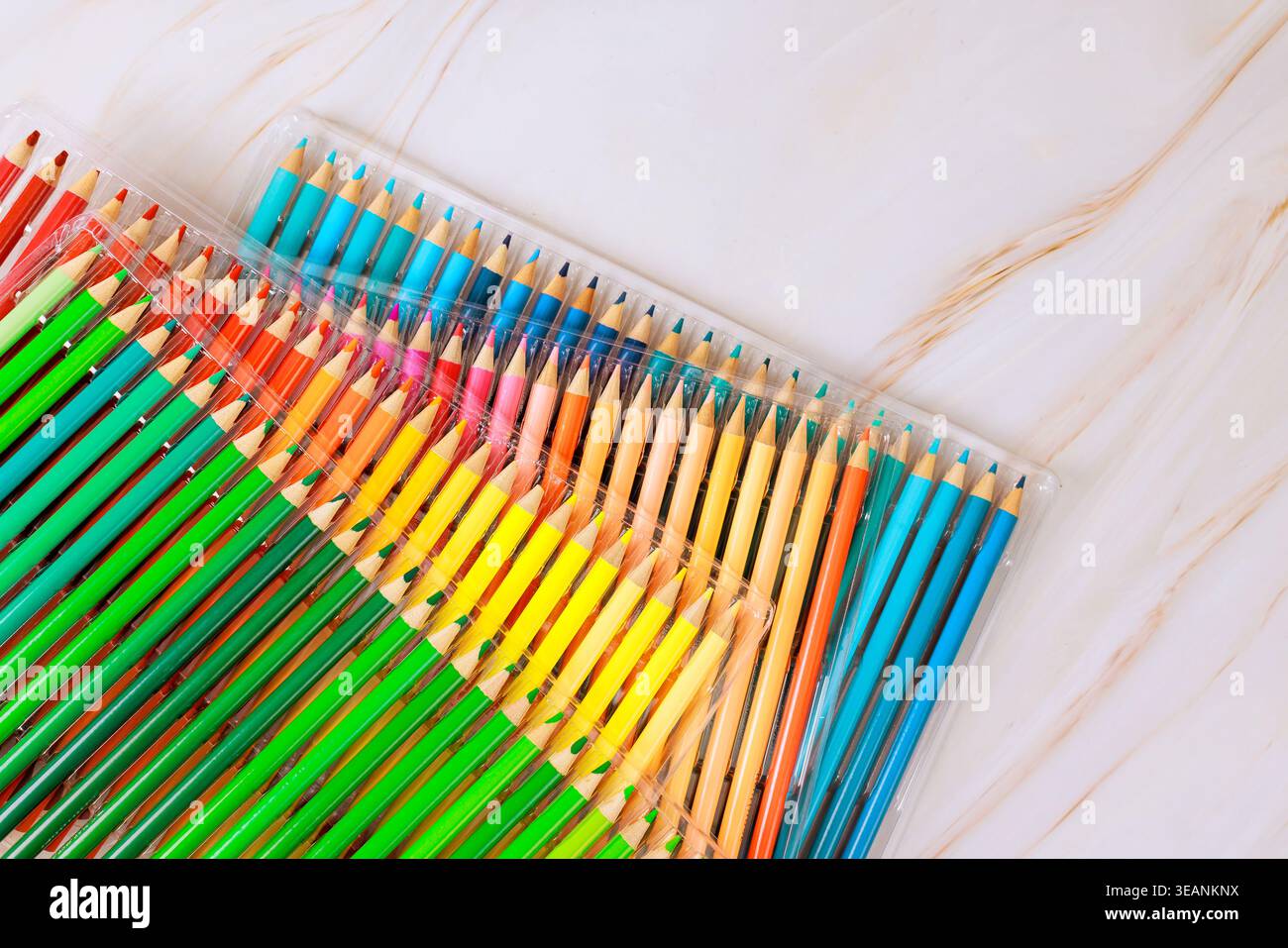 Crayons de couleur dans un emballage transparent assis sur une surface lisse, prêt pour le dessin, l'artisanat, les projets scolaires. Banque D'Images